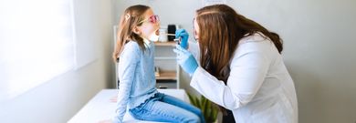 Female pediatrician examining young patient's throat with tongue depressor during a medical consultation 