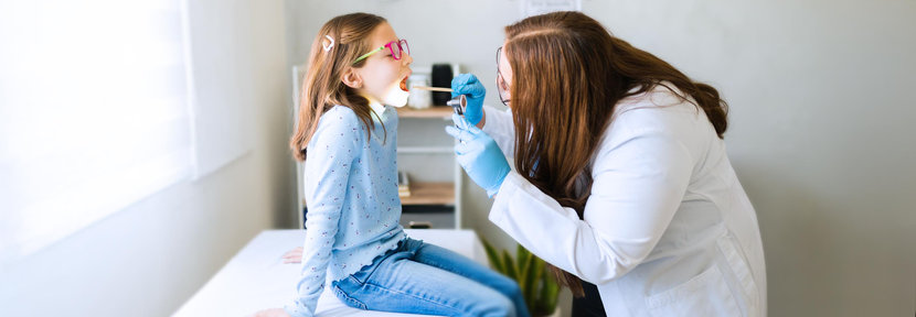 Female pediatrician examining young patient's throat with tongue depressor during a medical consultation 