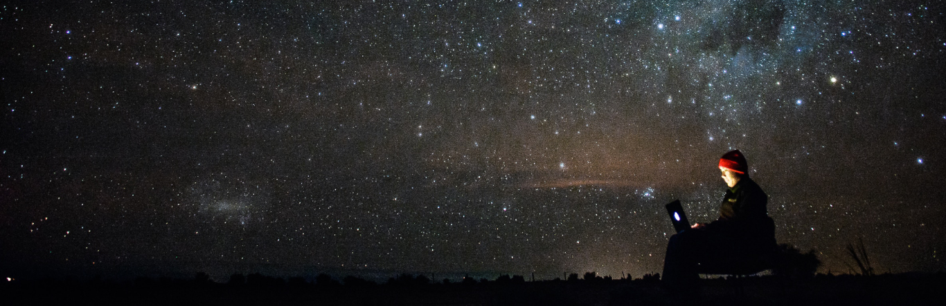 Person on their laptop outside in a starred filled night sky