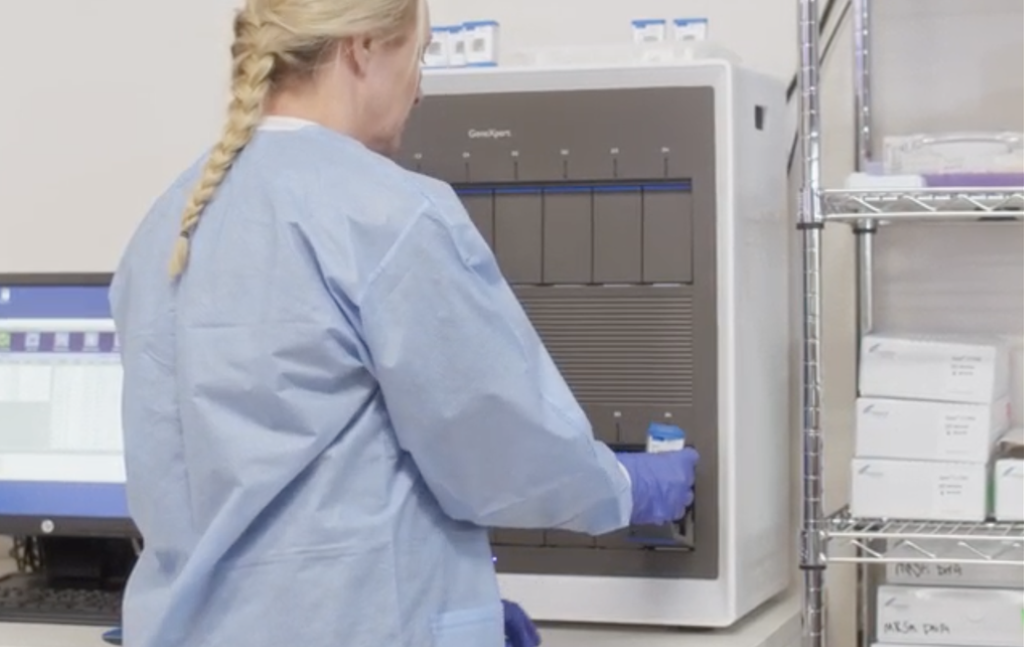 A laboratory worker putting a Cepheid Xpert cartridge in a GeneXpert system